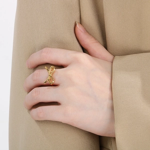 Close-up of a delicate gold bow-shaped stainless steel ring worn on a model's finger
