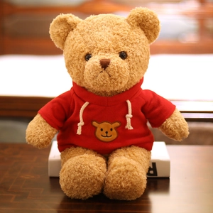 Cuddly brown plush teddy bear wearing a red drawstring hoodie on a warm wooden surface