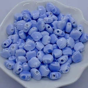 Macro detail of blue shell-shaped ceramic beads with holes in a white shell dish