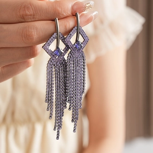 Detail of purple rhinestone fringe earrings with geometric diamond-shaped blue stone top
