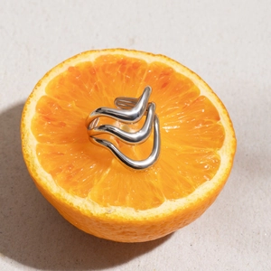 Detail of minimalist wavy multi-layer stainless steel ring set on an orange fruit