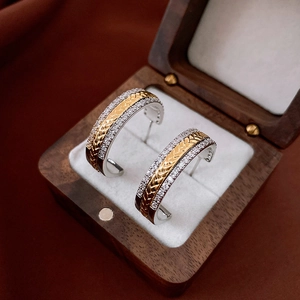Macro detail of 14K gold plated C-shaped earrings with zircon inlay in a wooden jewelry box