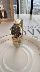 Close-up of a gold square women's watch with a black dial on a white ceramic plate