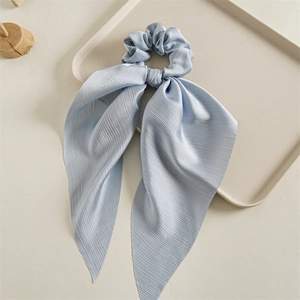 Close-up of a blue silk-texture hair scrunchie with long ribbon on a beige tray