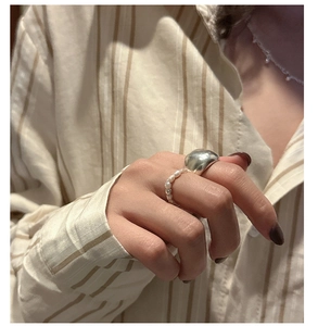 Close-up of stacked silver dome ring and pearl beaded ring on a neutral background