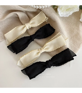 Close-up of four fabric bow hair clips in beige and black on elegant linen backdrop