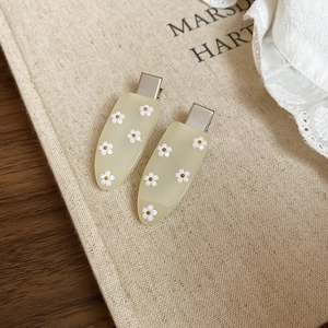 Detail of cream drop-shaped hair clips with white flower patterns and silver metal duckbill base