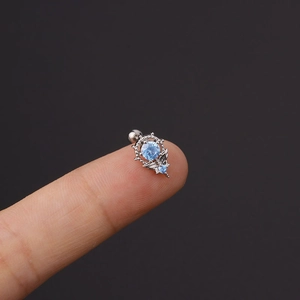 Makroaufnahme von Silberohrring mit hellblauem Zirkon und Flügeln an der Fingerspitze