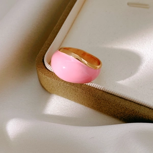 Macro detail of a wide gold-plated ring with pink enamel finish on white silk background