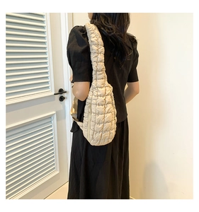 Sac nuage matelassé crème porté à l'épaule avec une robe noire élégante et fermeture éclair
