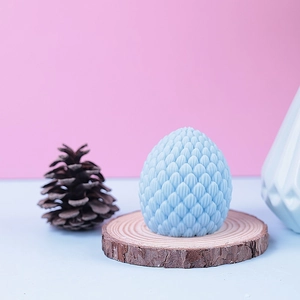 Creative blue dragon egg candle with scale texture on wooden base with pine cone