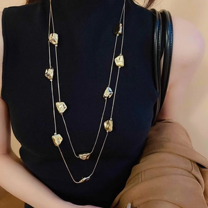 Dettaglio della collana dorata a doppio strato con ciondoli geometrici su una modella
