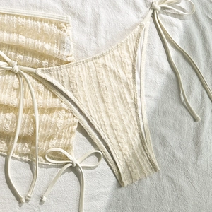 Detail eines cremeweißen Spitzen-Bikini-Sets mit feinen floralen Häkelmustern und Bändern