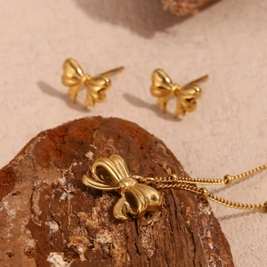 Close-up of gold bow necklace and earrings on wood texture with soft lighting