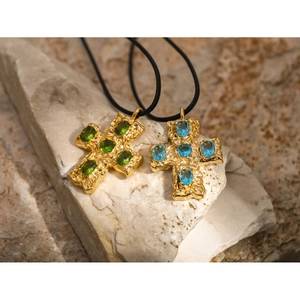 Macro detail of 18k gold cross pendants with green and blue gems on natural rock