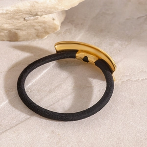 Minimalist black hair tie featuring a polished gold curved metal accent on stone background