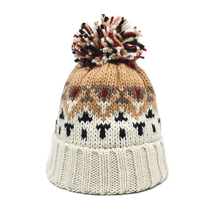 Detail of winter knit beanie with colorful pompom and geometric jacquard pattern