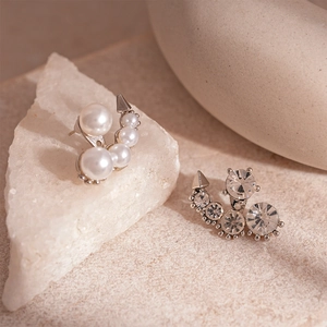 Asymmetric silver earrings with pearls and rhinestones on a minimalist stone background