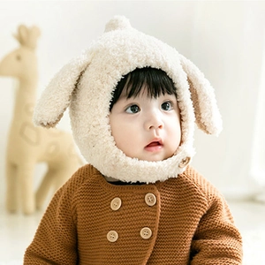 Close-up of beige plush baby hat with cute rabbit ears on a baby wearing brown cardigan