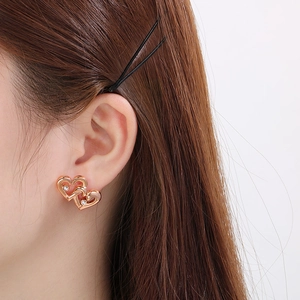 Close-up of interlocking rose gold heart earrings with zircon stones worn on the ear