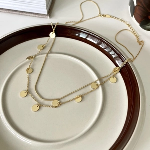 Close-up of double-layer gold necklace with small round sequins on a ceramic tray