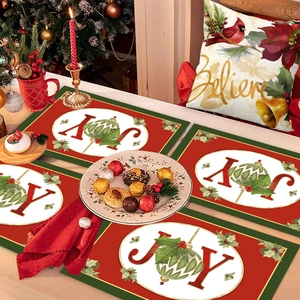 Set of 4 red and green JOY Christmas placemats with holly leaf patterns on a dining table
