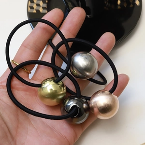 Detailed close-up of metallic brushed gold ball hair tie held in hand for scale