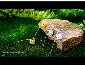 Detail of creative rotating windmill earrings in silver and gold on natural grass