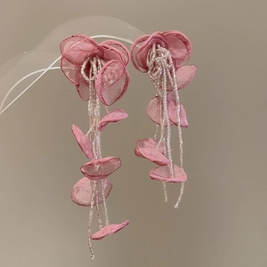 Detailed close-up of pink fabric flower tassel earrings on a clear jewelry display stand