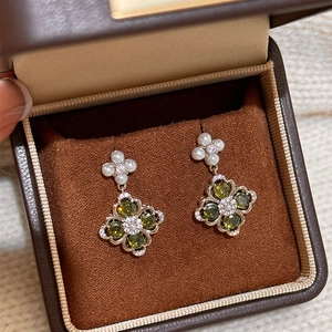 Detail of silver clover earrings with green gemstones and pearls in a leather box