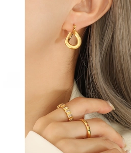 Detail of twisted gold earrings and sparkling zircon rings on female model