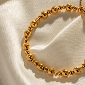 Makroansicht des polierten 18K Gold-Edelstahl-Perlenarmbands auf Seidenstoff