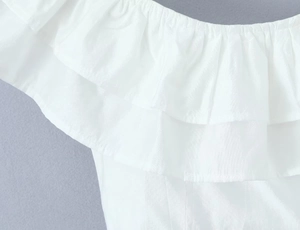 Detailed macro shot of white ruffled off-shoulder top showing woven fabric textures