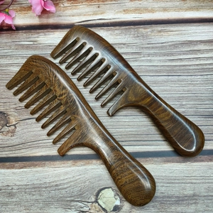 Set of two wide-tooth black gold sandalwood massage combs on a textured wood surface
