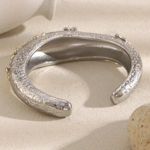 Handcrafted silver hammered cuff bracelet with gold floral accents on stone surface