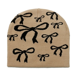 Detail of beige knit beanie featuring black bow jacquard pattern and textured wool material