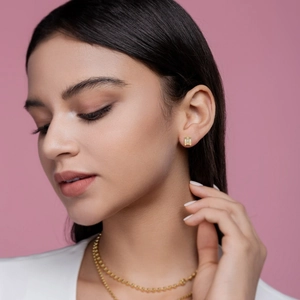 Elegant gold square stud earrings with sparkling stones worn by a model on pink background