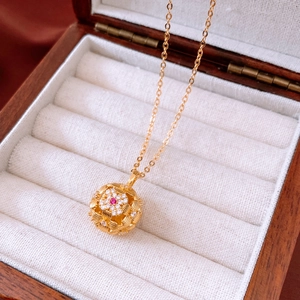 Close-up of golden vintage necklace with hollow sphere pendant and red gemstone inlay