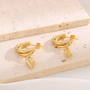 Polished gold heart drop earrings with double rings on a textured stone display