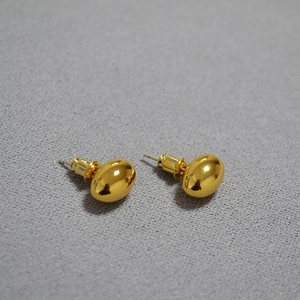 Macro shot of polished gold oval stud earrings with reflective metallic finish and mirror effect