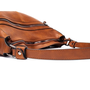 Detailed close-up of brown textured leather crossbody bag with multiple zippers