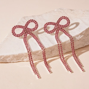 Gros plan détaillé des boucles d'oreilles nœud rose en strass avec pompons sur pierre
