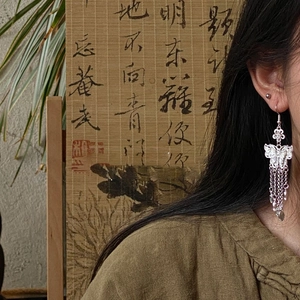 Detail of silver hollow butterfly tassel earring with delicate metal chains on model