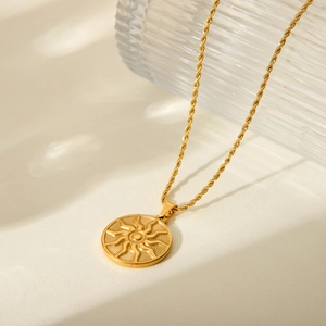 Close-up of golden sun totem pendant necklace with twisted rope chain on textured glass