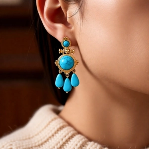 Detail of vintage gold earrings with turquoise stones and textured relief dangles on a model
