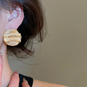 Gros plan de boucles d'oreilles dorées avec texture métallique froissée sur l'oreille