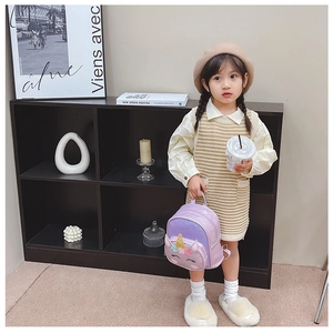 Toddler girl wearing a purple unicorn backpack with sequins in a modern home setting