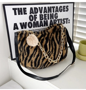 Detail of plush tiger print tote bag featuring a gold chain and a pink pompom charm