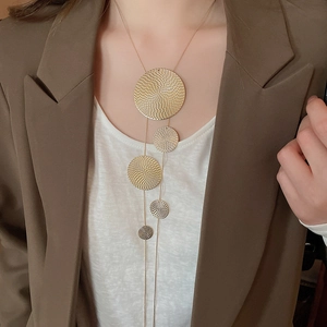Detail of long gold necklace with textured circular metal pendants on model