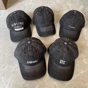 Detail of five washed denim baseball caps with various letter embroidery on grey background